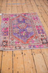 Distressed vintage Oushak rug, low pile showing geometric motifs in purple, pink, and terra cotta.
