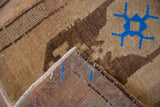 Folded vintage Oushak mat revealing distressed brown pile with blue motif and woven back.