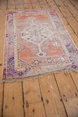 Distressed Oushak rug corner, fringed with geometric terracotta and purple-blue patterns.