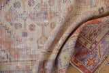 Faded ivory, terra cotta, and purple geometric motifs on a distressed vintage Oushak rug with fringe.