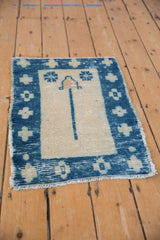 Angled view of distressed vintage Oushak mat, aged ivory texture, cobalt blue plant and geometric motifs.