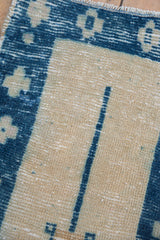 Distressed Oushak rug close-up: pale ivory, cobalt geometric pattern, with visible pile wear.