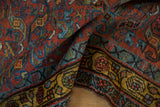 Folded vintage Kurdish Bijar rug detail with spiraled floral gem-tone pattern and saffron yellow border.