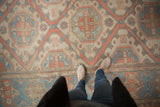 Distressed Soumac carpet detail showing reciprocating geometric medallions in muted coral, blue, and ivory.