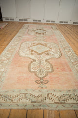 Distressed vintage Oushak runner end, geometric border, and heavily abrashed dusty rose field.