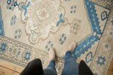 Distressed ivory and indigo blue Oushak carpet, highlighting the scalloped medallion and floral pinwheels.