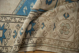 Distressed Oushak carpet detail with ivory texture, indigo blue florals, and starburst border.