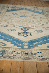Distressed ivory and indigo blue Oushak rug corner, showing pinwheel florals and palmette border.
