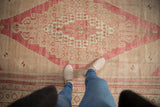 Distressed vintage Oushak rug with a central stepped medallion, featuring raspberry and sand tones, underfoot.
