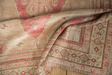 Distressed Oushak rug detail: geometric borders, pinwheel design, and abrashed field in raspberry and beige.