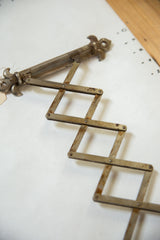Antique Fleur de Lis shaving mirror's accordion extension, displaying darkened patina and rust.
