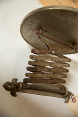 Antique shaving mirror's accordion mechanism and fleur de lis hardware, showing darkened patina.