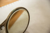 Close-up of antique mirror's circular glass, showing spots and darkened frame patina.