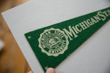 Close-up of vintage Michigan State University seal on green felt pennant.
