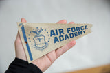Close-up of vintage Air Force Academy felt pennant with blue emblem and visible wear.