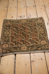Angled view of a distressed Farahan Sarouk mat with an intricate floral field and wide coffee-toned border.