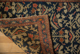 Hand-knotted Farahan Sarouk rug's folded corner, revealing dense weave and indigo, beige, red pattern.
