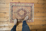 Top-down view of an antique Kerman square mat, shown for scale on a floor.