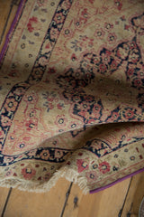 Folded antique Kerman rug revealing its purple side cord, low pile, and ivory fringe.