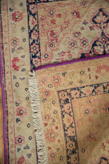 Corner of an antique Persian rug showing its purple side cord, short ivory fringe, and foundation.