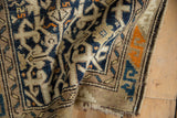 Folded Caucasian rug with cobalt blue, beige geometric patterns, tangerine border, and tattered end.