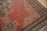 Distressed pile of a vintage Senneh rug showing dusty copper abrashed field and charcoal vine border.