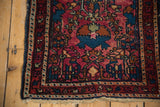 Bottom corner of vintage Lilihan rug, raspberry field, blue motifs, and varied pile.
