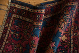 Curved vintage Lilihan rug detail reveals sapphire blue and ruby red floral motifs with varying pile.