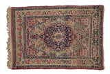 Antique Kerman rug with a starburst medallion in navy blue and red over a sand-colored millefleur ground.