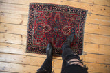 A person's view of a vintage Sarouk rug's dense floral field in red and indigo blue.