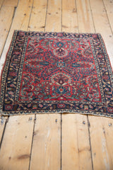 Full view of a vintage German Sarouk rug from an angle, showcasing the raspberry red floral field.