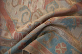 Distressed Soumac carpet folded, highlighting geometric floral motifs, dusty rose, and sky blue abrash.