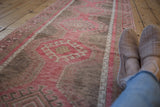Angled perspective of a distressed Oushak runner with raspberry red and sand medallions.