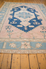 Distressed vintage Oushak rug with cobalt blue stepped medallion, dusty blush field, and primitive floral motifs.