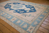 Distressed Oushak rug corner, dusty blush field, and faded powder blue floral border.