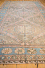 Distressed Soumac rug border detail featuring blue floral motifs and geometric patterns in dusty rose.