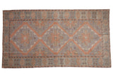 Distressed vintage Soumac carpet featuring triple diamond medallions in blush, powder blue, and mauve.