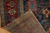 Folded Malayer rug corner, showing hand-knotted foundation and worn red, navy floral motifs.