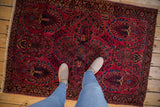 Vintage American Sarouk rug: raspberry red field with indigo floral motif, light shoes on surface.