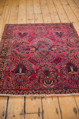 Vintage Sarouk rug corner with raspberry red floral sprays, indigo vases, and fringe.