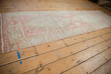 Corner of a distressed Oushak runner showcasing worn texture, faded pink designs.
