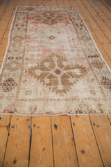 Fringed end of the distressed Oushak rug, showing faded blush, ivory, and low-pile patterns.