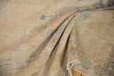 Textured detail of distressed vintage Oushak carpet, showing worn beige pile, pale blue and green motifs.