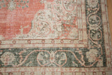 Distressed vintage Sparta carpet corner, dusty terra cotta with deep green meandering vine border.