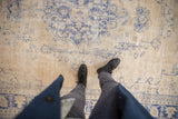 Distressed Oushak rug underfoot, with faded cobalt blue scrolling vines on a light beige ground, showing low pile.