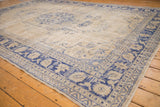 Distressed vintage Oushak rug corner, cobalt blue meandering vine border, and faded beige field.
