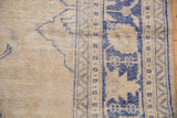 Distressed vintage Oushak rug, showing worn beige pile, visible foundation, and cobalt blue border.
