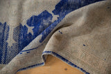 Blue side selvage, worn pile, and hand-knotted foundation of a distressed vintage rug.