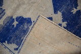 Distressed Oushak rug corner with worn pile, exposed foundation, blue selvage, and reverse markings.