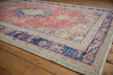 Distressed vintage Oushak carpet corner with navy blue border and faded floral field.